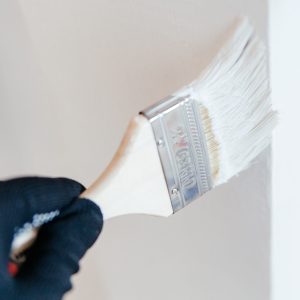 Close-up of a worker's hand with a brush painting a wall with white paint. Painting apartment, renovating with white color paint.